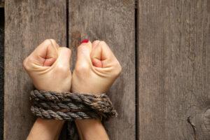 Tied female hands with rope on wooden background to illustrate human trafficking.