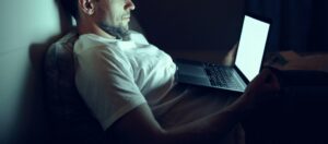 Man lying in bed using a laptop late at night, with a glowing screen symbolizing digital dependence.