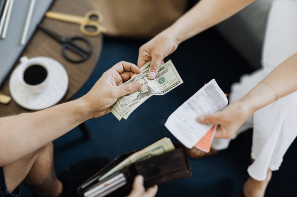 Close-up of hands exchanging U.S. dollar bills and a receipt, depicting a transaction involving counterfeit money.