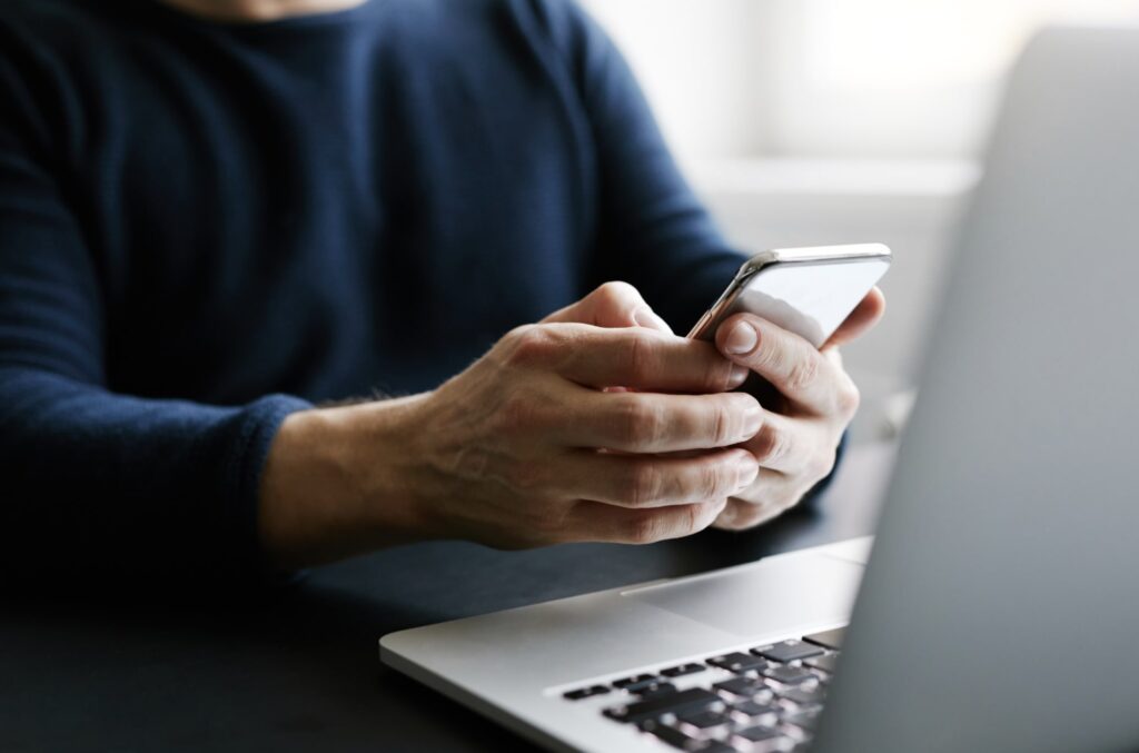 Person using a smartphone near a laptop, symbolizing creation or sharing of deep fake content
