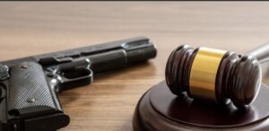 A judge's gavel lying across a crossed-out silhouette of a firearm.